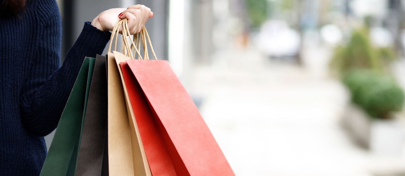 Women holding shopping bags outside. One bag is brown and the other is red.