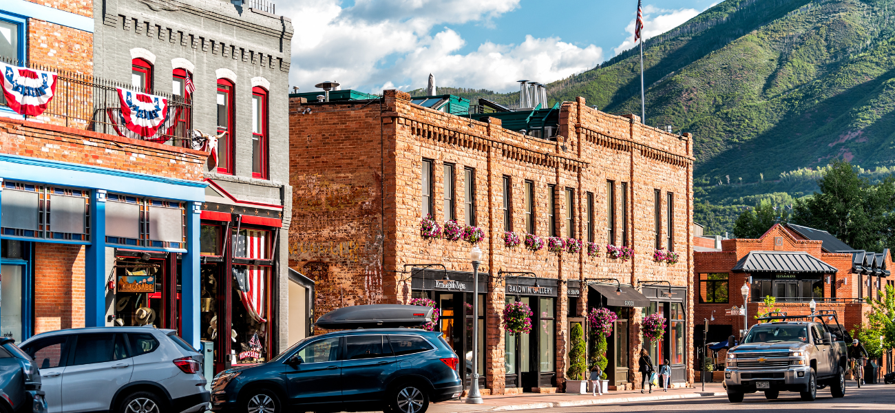 A bustling summer scene on S Galena Street in Aspen, with colorful storefronts and pedestrians enjoying the sunny weather