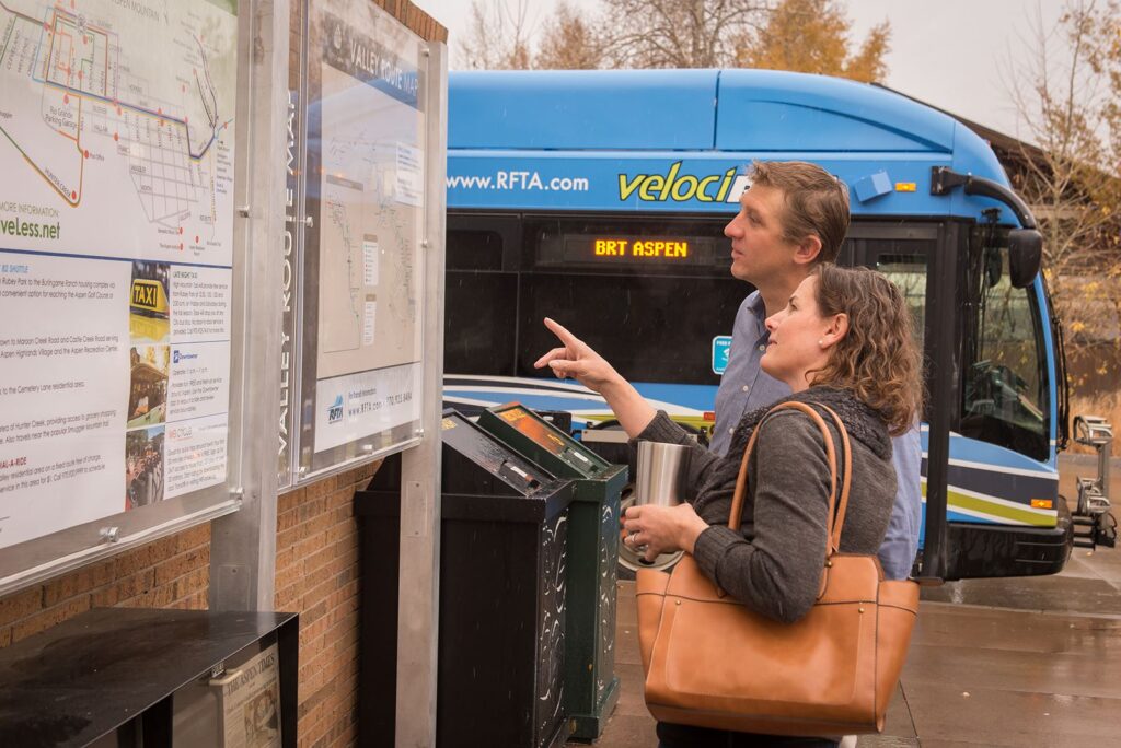 Man and women stand at information board in Brush Creek, Woody Creek, Aspen Colorado. A sustainable RAFTA bus is in the background. 